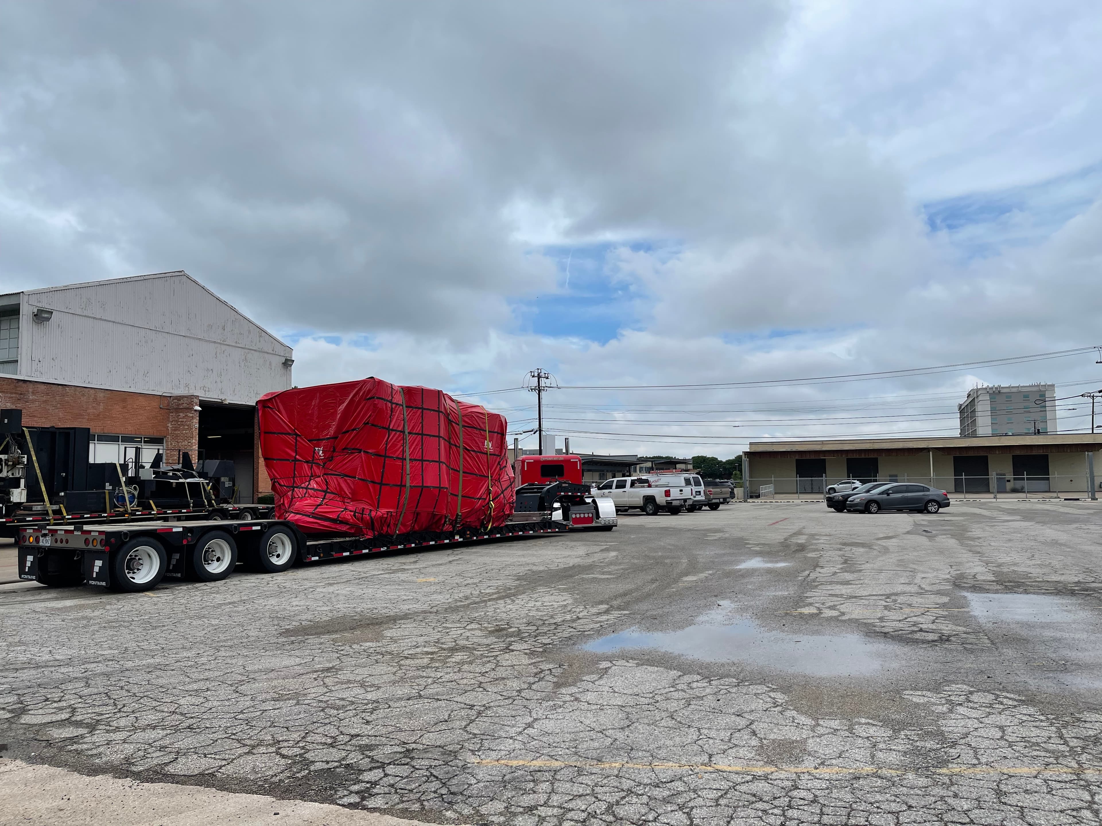 Red tractor hauling a tarped oversize load on a multi-axle lowboy trailer